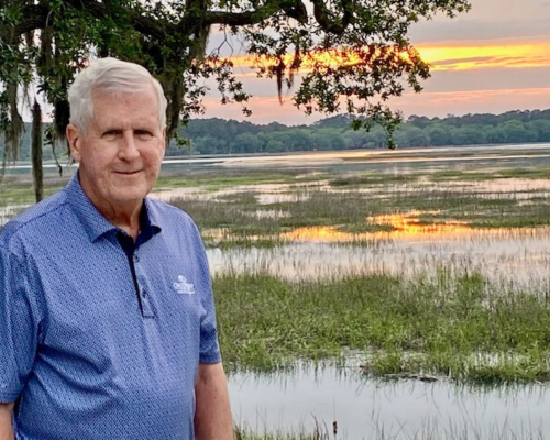 A man stands in front of a tree at sunset.