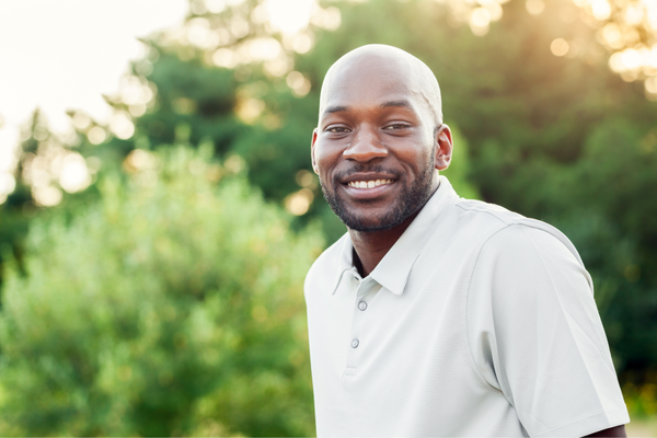 A man smiles outdoors in front of trees.