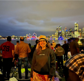 A woman smiles in a crowd of people against the Sydney, Australia skyline waiting for New Year's Eve fireworks.
