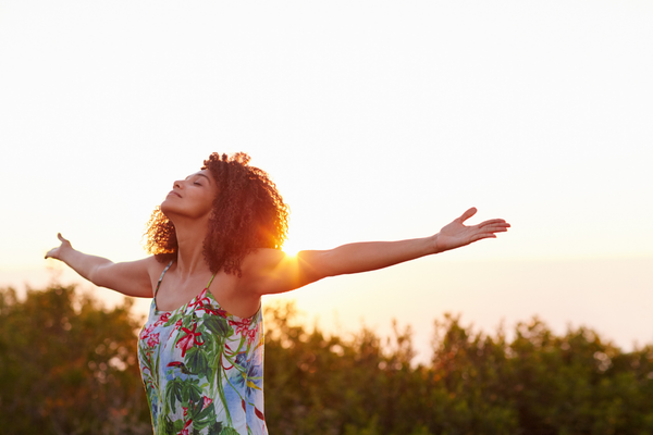 A woman looks up at the sky and holds her arms out in a confident pose.