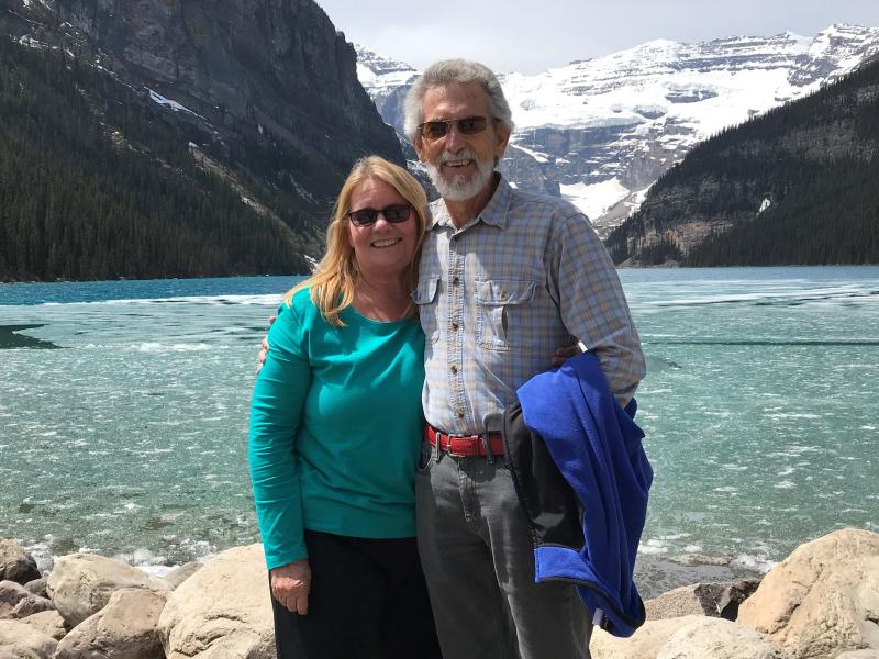 Photo of a smiling couple standing in front of a hot spring. The couple is Mary and Paul McQueen.