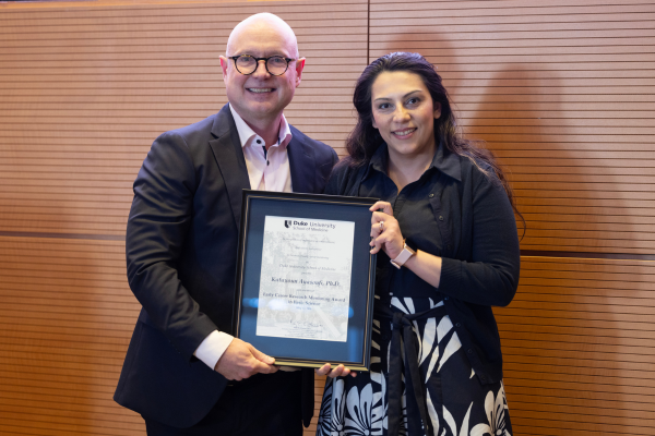 Two adults smile and pose with an award.