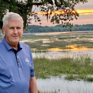 A man stands in front of a tree at sunset.